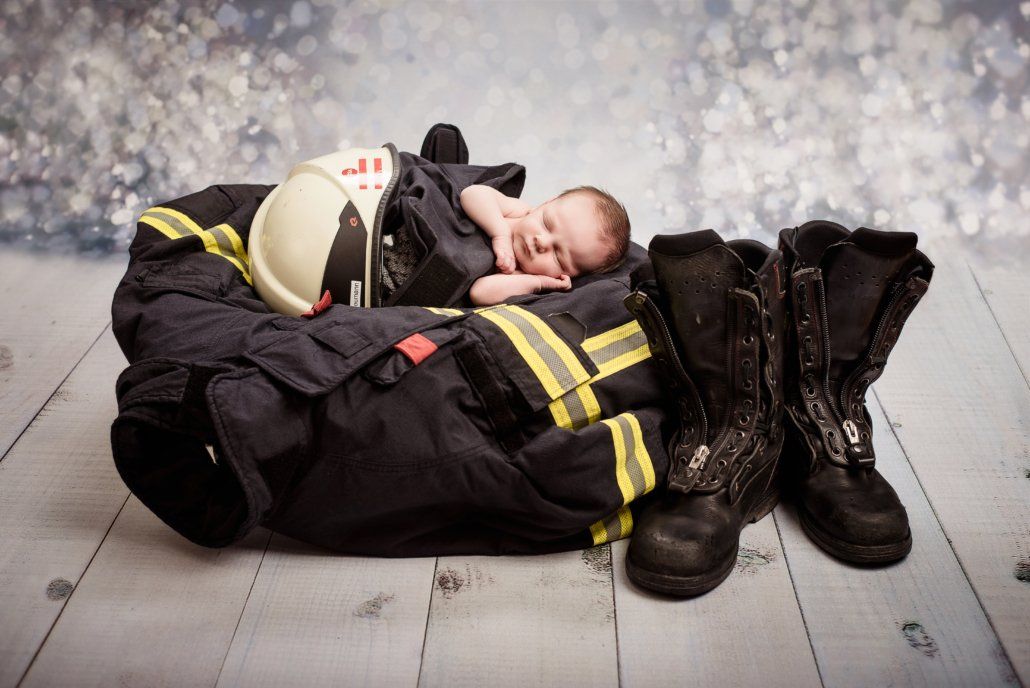 Ein Baby schläft in einem Feuerwehranzug und Stiefeln.