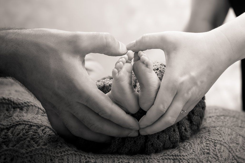 Auf einem Schwarzweißfoto hält eine Person die Füße eines Babys in ihren Händen.