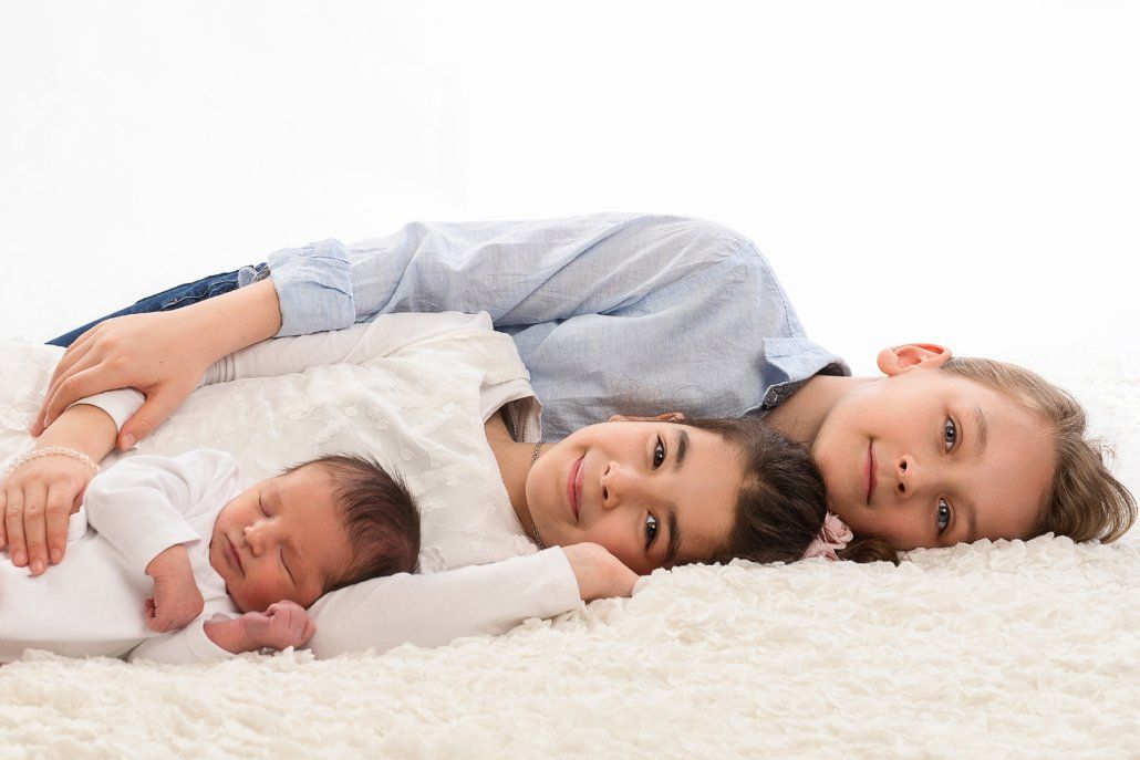 Drei Kinder liegen mit einem Neugeborenen auf einem Teppich.