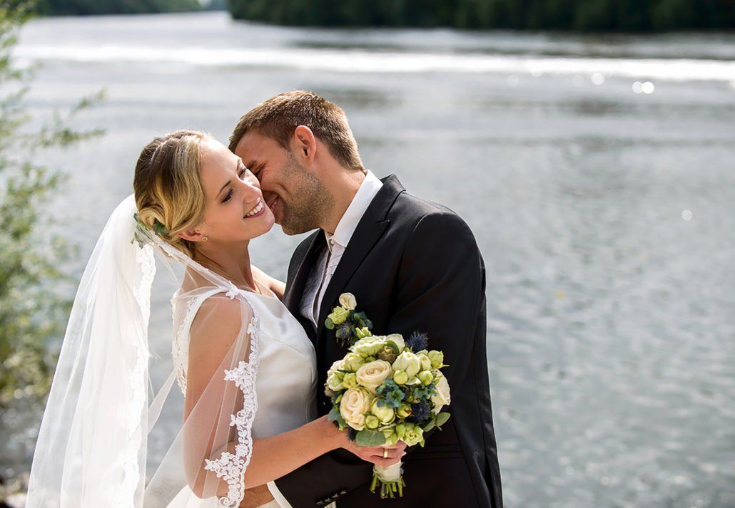Eine Braut und ein Bräutigam küssen sich vor einem See.