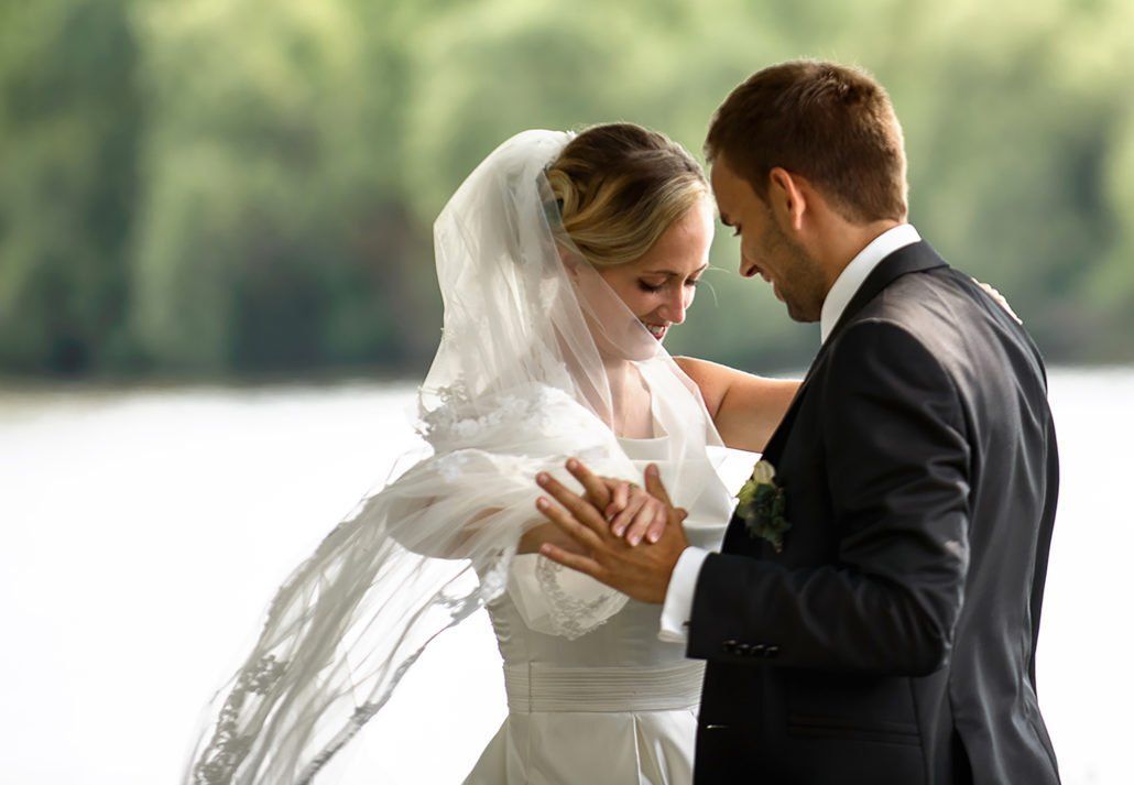 Eine Braut und ein Bräutigam tanzen vor einem See.
