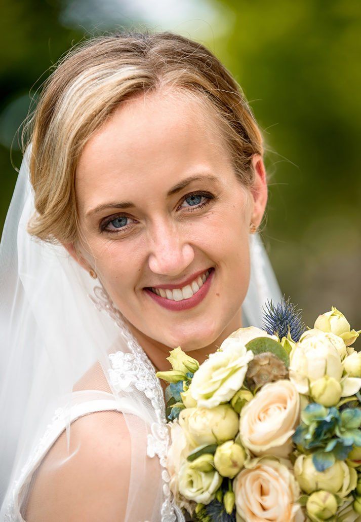 Die Braut lächelt und hält einen Blumenstrauß.