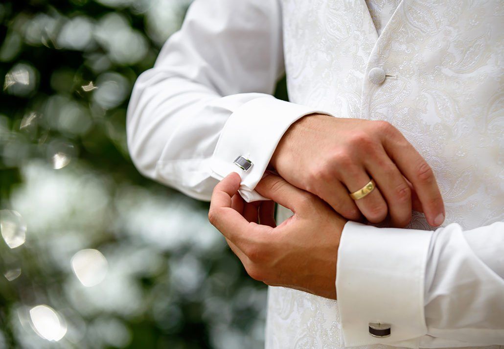 Ein Mann mit einem Ehering rückt seine Manschettenknöpfe zurecht