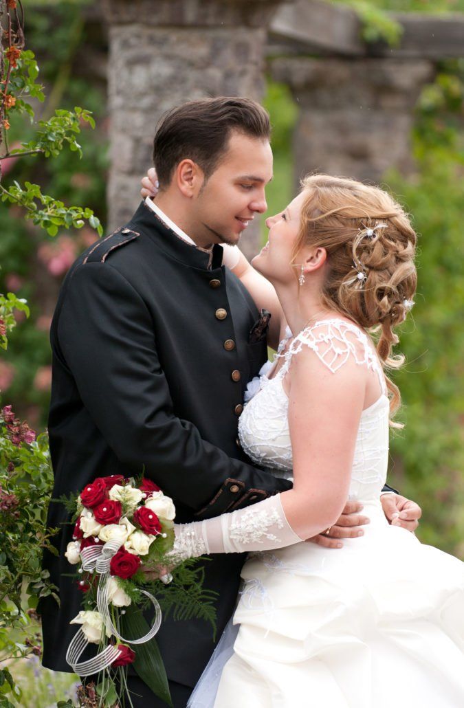 Eine Braut und ein Bräutigam küssen sich vor einer Steinmauer.