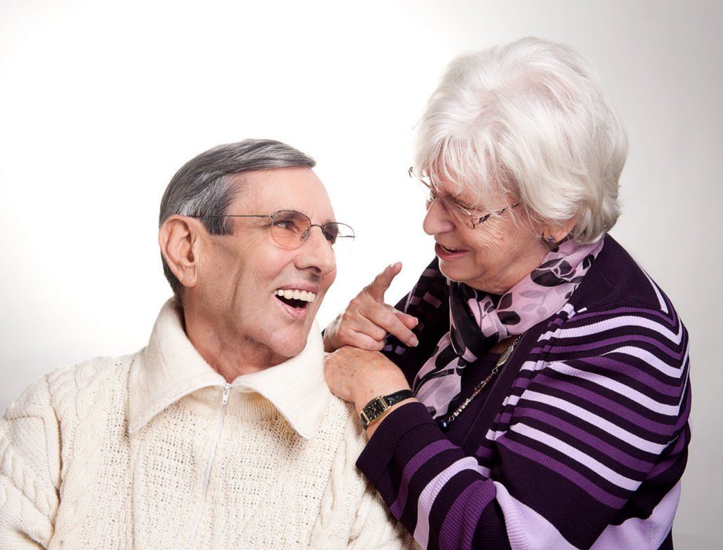 Ein älterer Mann und eine ältere Frau lachen zusammen und die Frau zeigt auf das Gesicht des Mannes