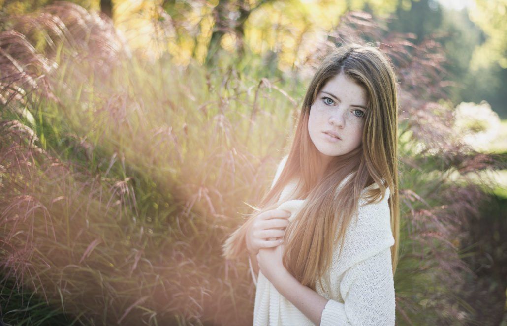 Eine junge Frau in einem weißen Kleid steht auf einem Feld mit hohem Gras.