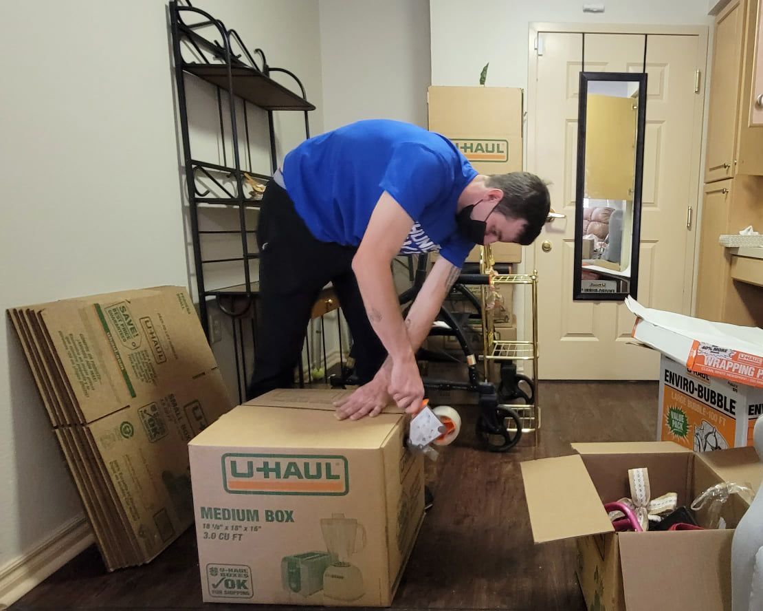A man in a blue shirt is wrapping a u-haul box
