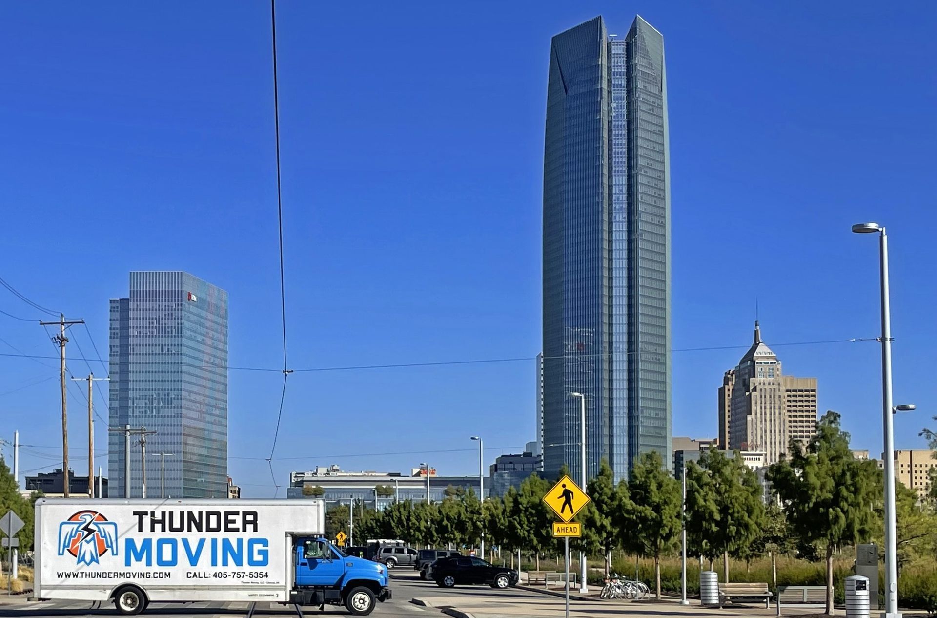 A Thunder Moving truck is driving in downtown Oklahoma City with Devon Energy Center in the background.
