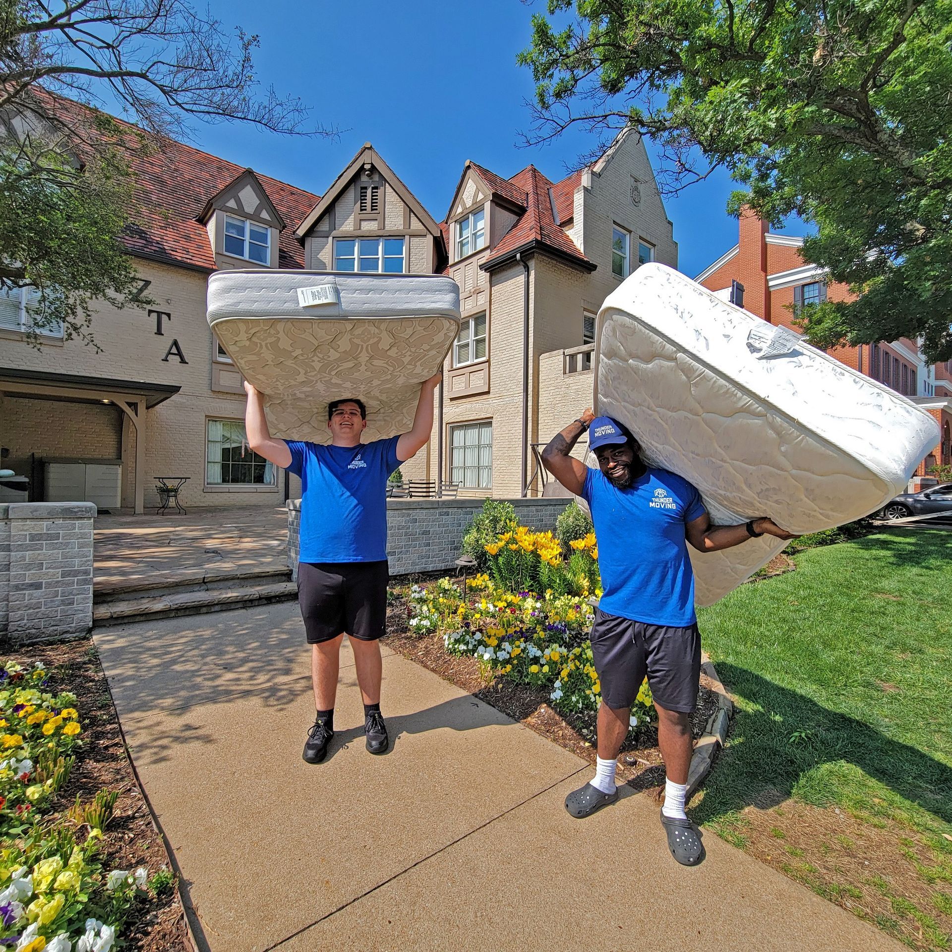 Two men are carrying a large mattress on their shoulders.