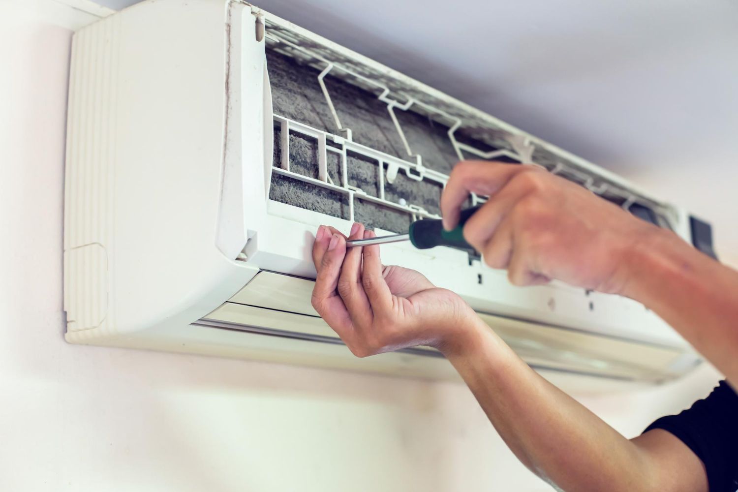 A technician uses a screwdriver to repair a wall-mounted air conditioning unit.