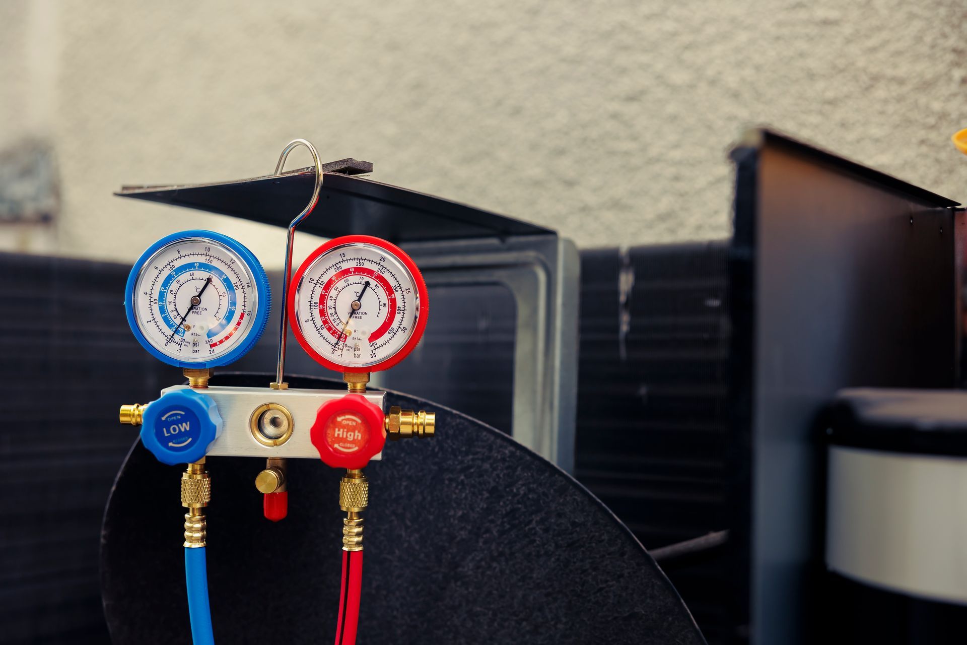 Refrigeration gauges, blue and red, attached to a metal unit with black and white components.