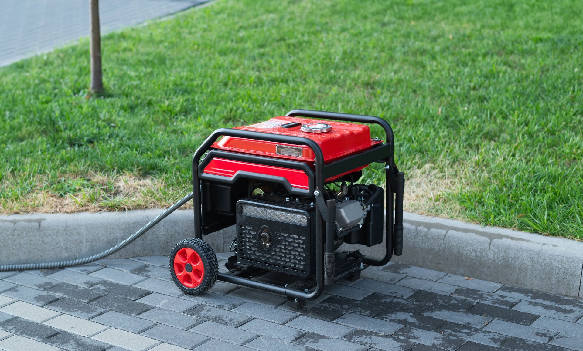 Red and black portable generator on a paved surface near green grass.