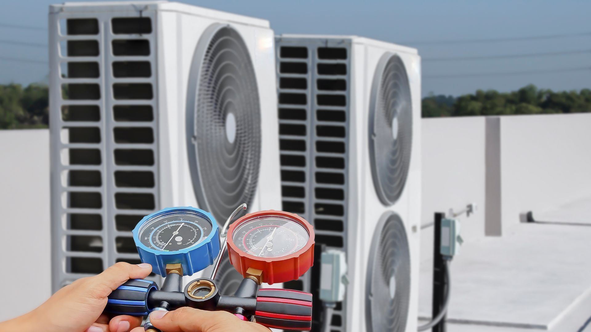A person is holding a pressure gauge in front of a row of air conditioners.