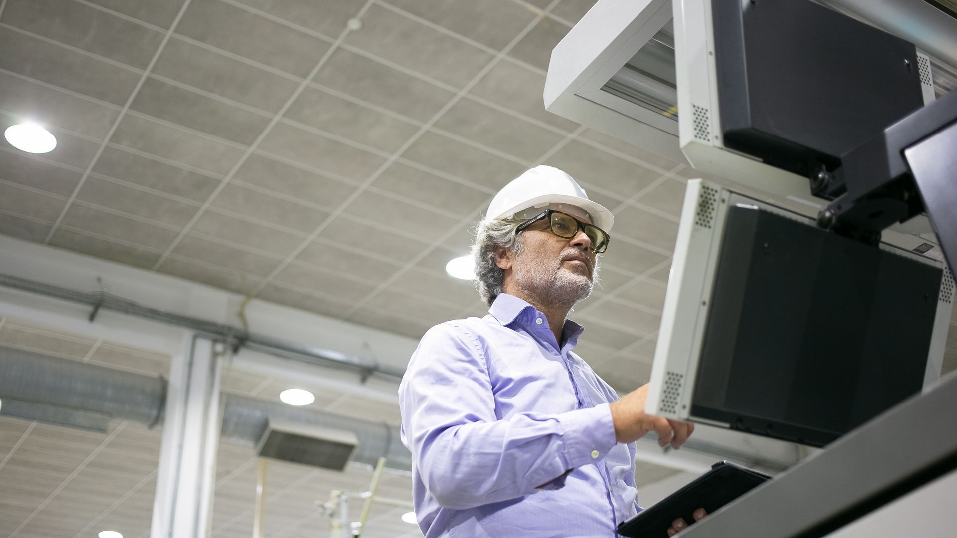 A man wearing a hard hat and goggles is working on a computer in a factory.