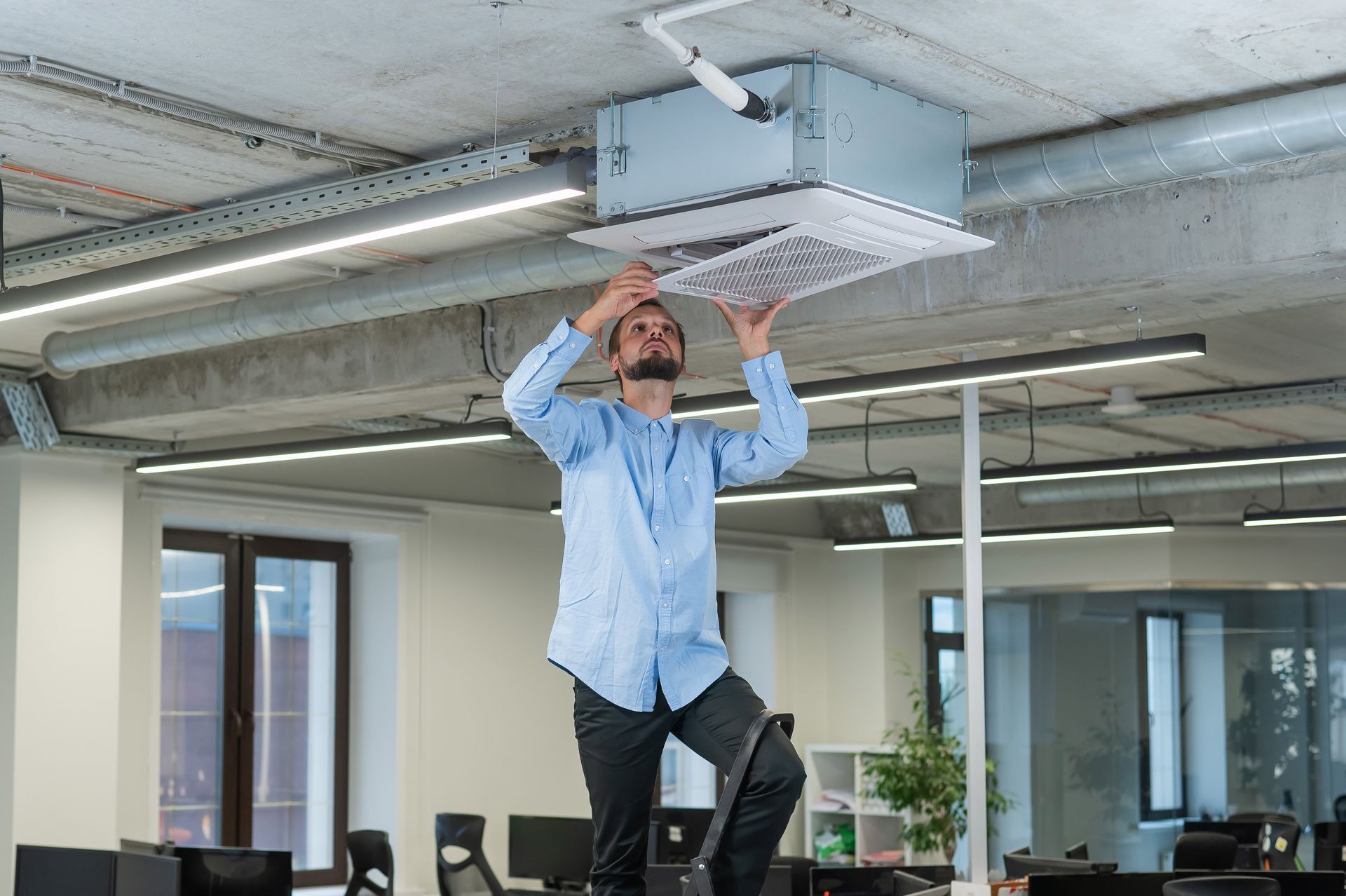 A man is fixing a ceiling fan in an office.