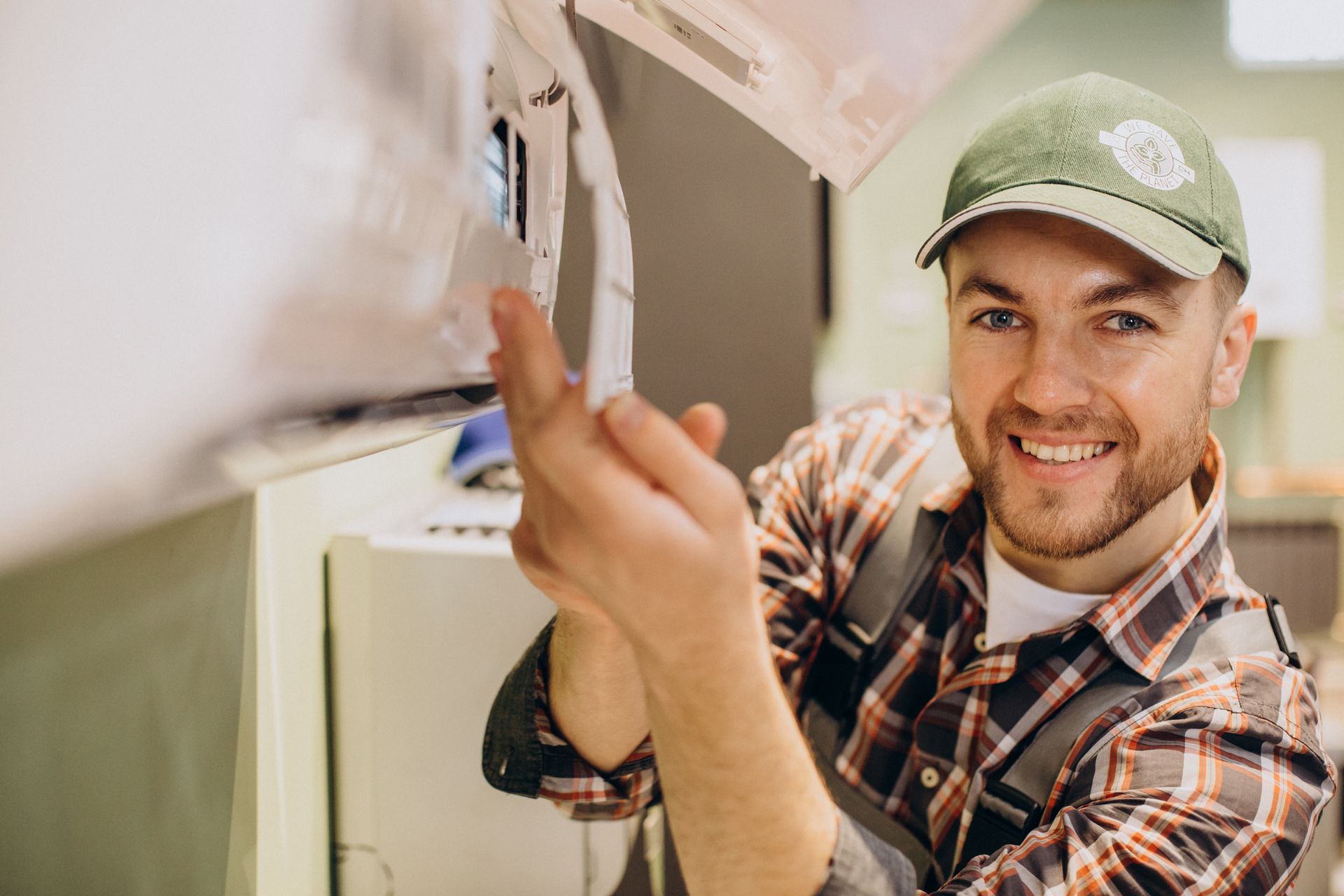 A man in a plaid shirt and hat is fixing an air conditioner.