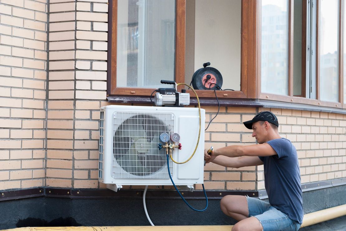 A man is installing an air conditioner on the side of a building.