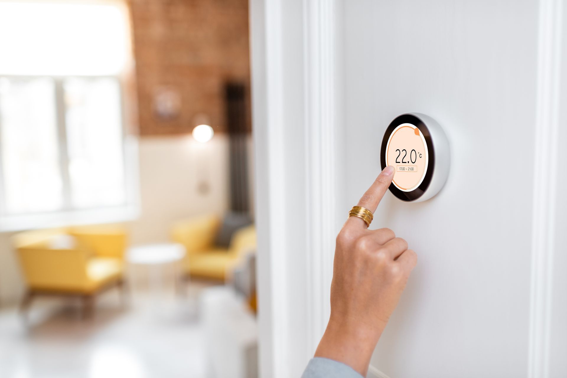 A person is pressing a button on a thermostat in a living room.