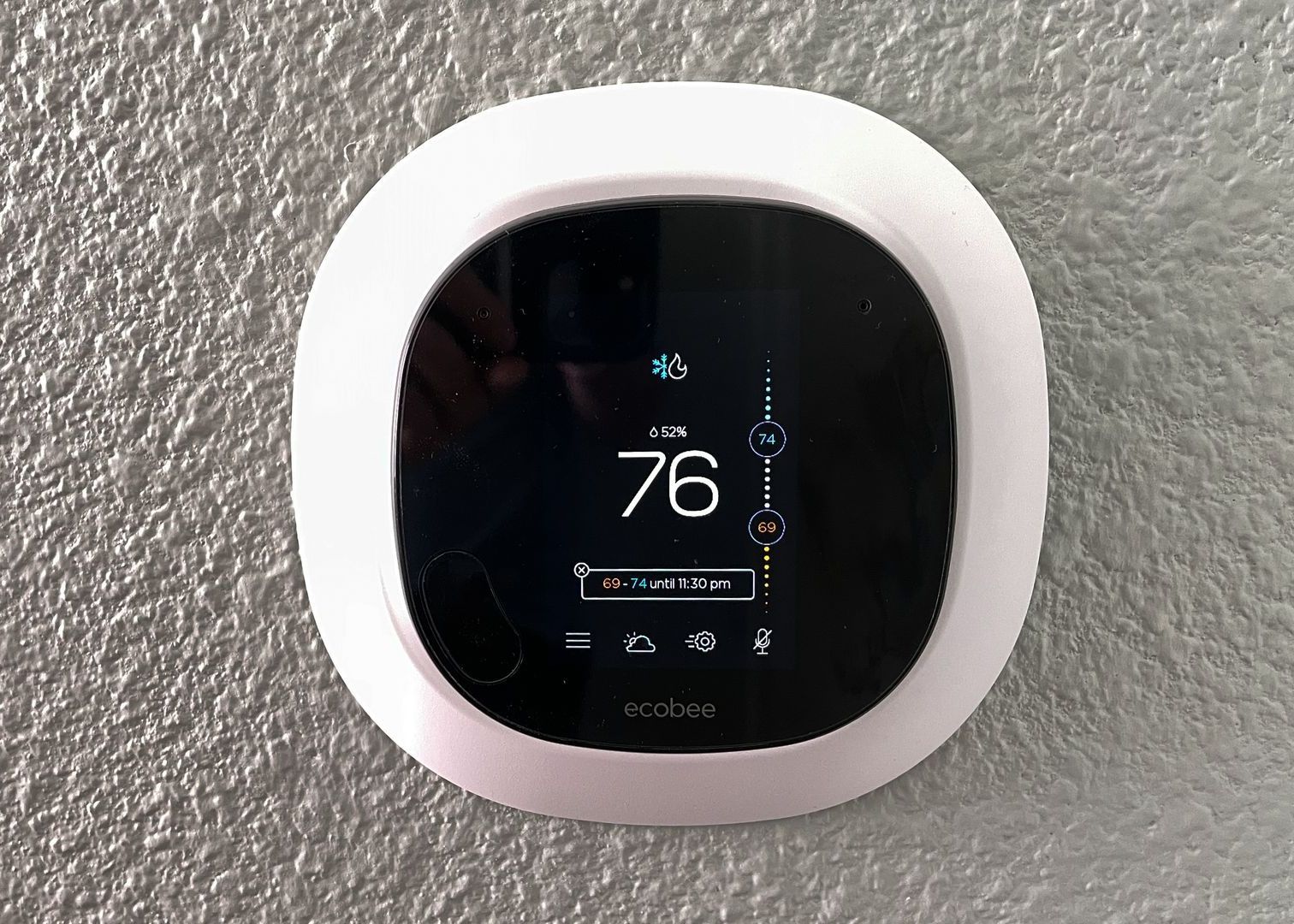 A smart thermostat is hanging on a wall and the temperature is 76 degrees.