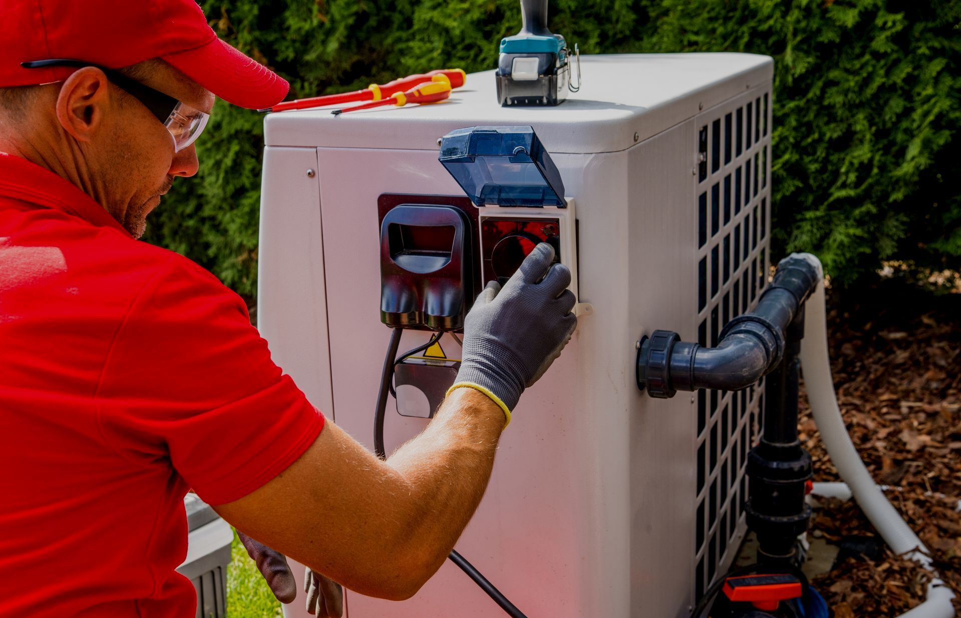 A man in a red shirt is working on a pool heater.