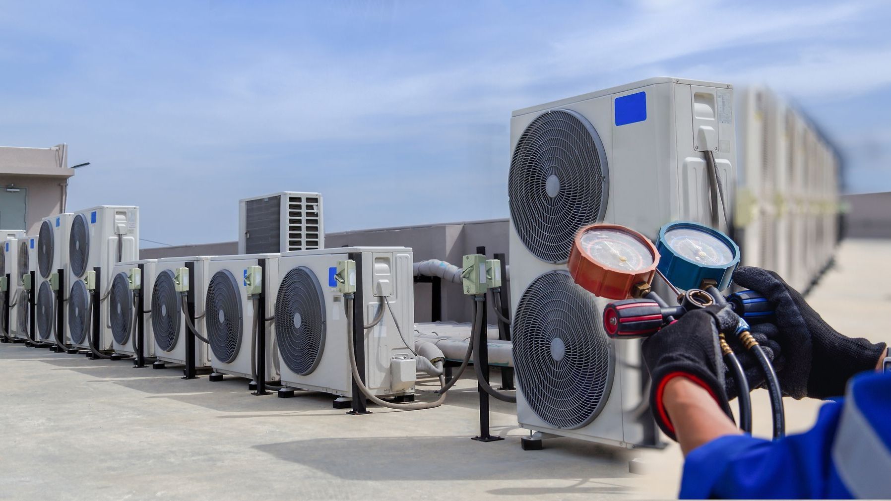 A man is holding a gauge in front of a row of air conditioners.