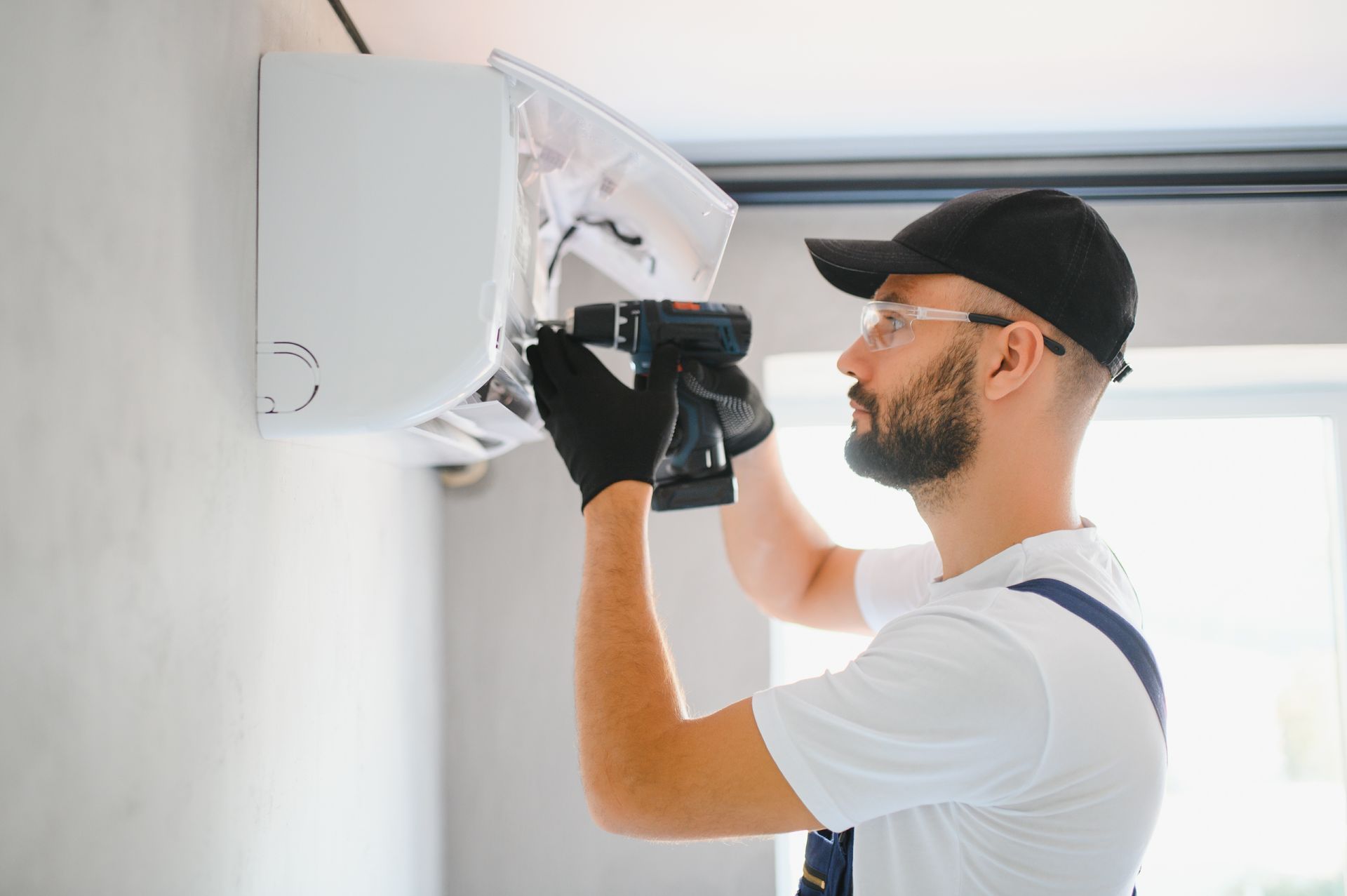 A man is fixing an air conditioner with a drill.