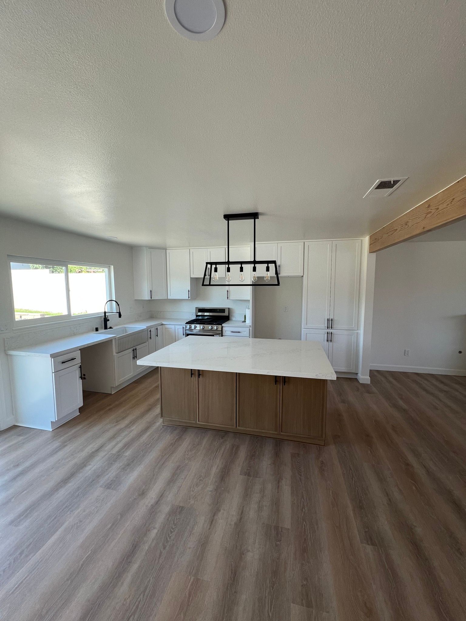Bright kitchen with island, white countertops, and wood-toned cabinets. Includes stove and window.