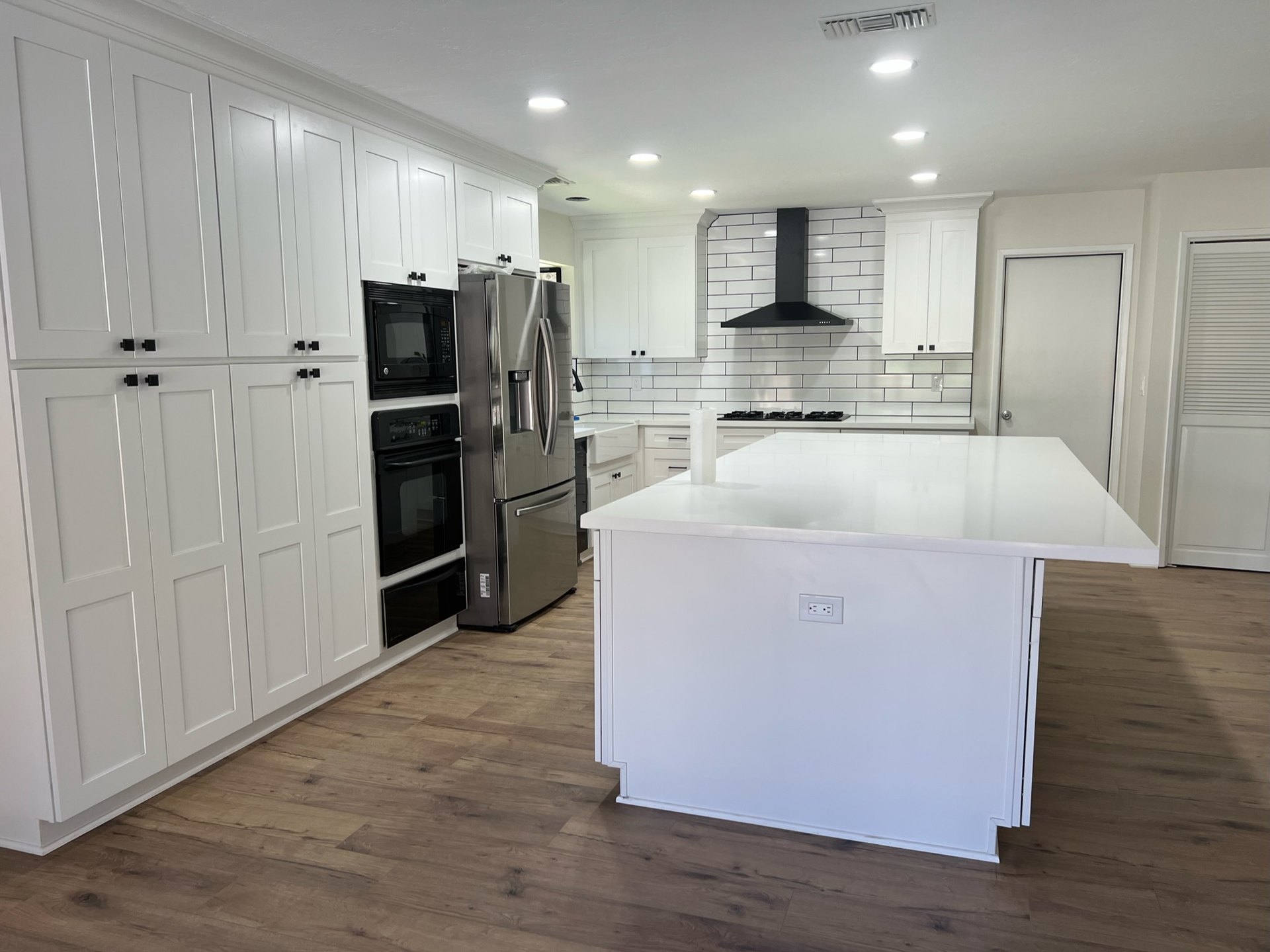 Spacious modern kitchen with white cabinets, island, stainless steel appliances, and wood floors.