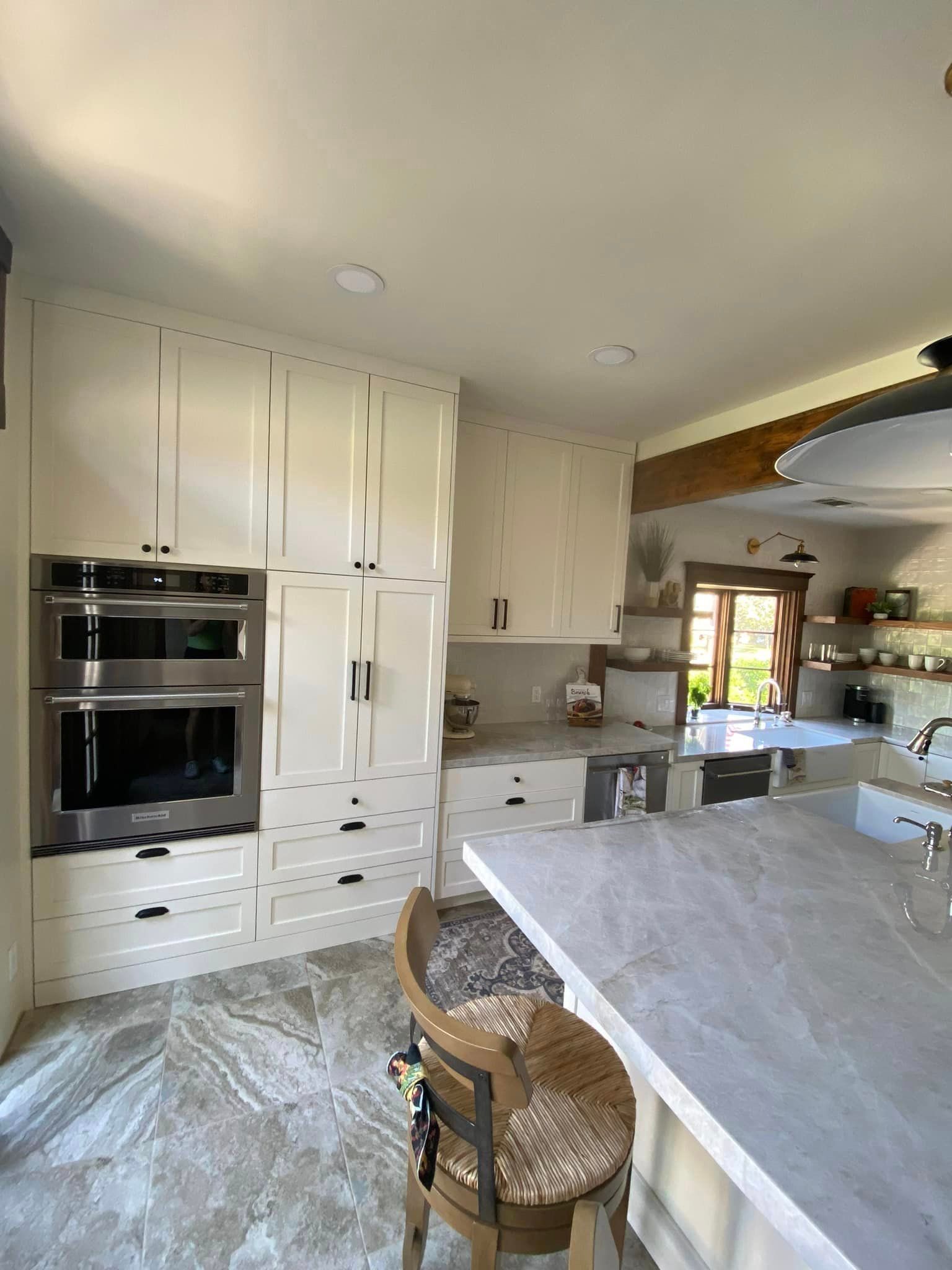 Bright kitchen with white cabinets, stainless steel oven, marble island, and patterned tile floor.