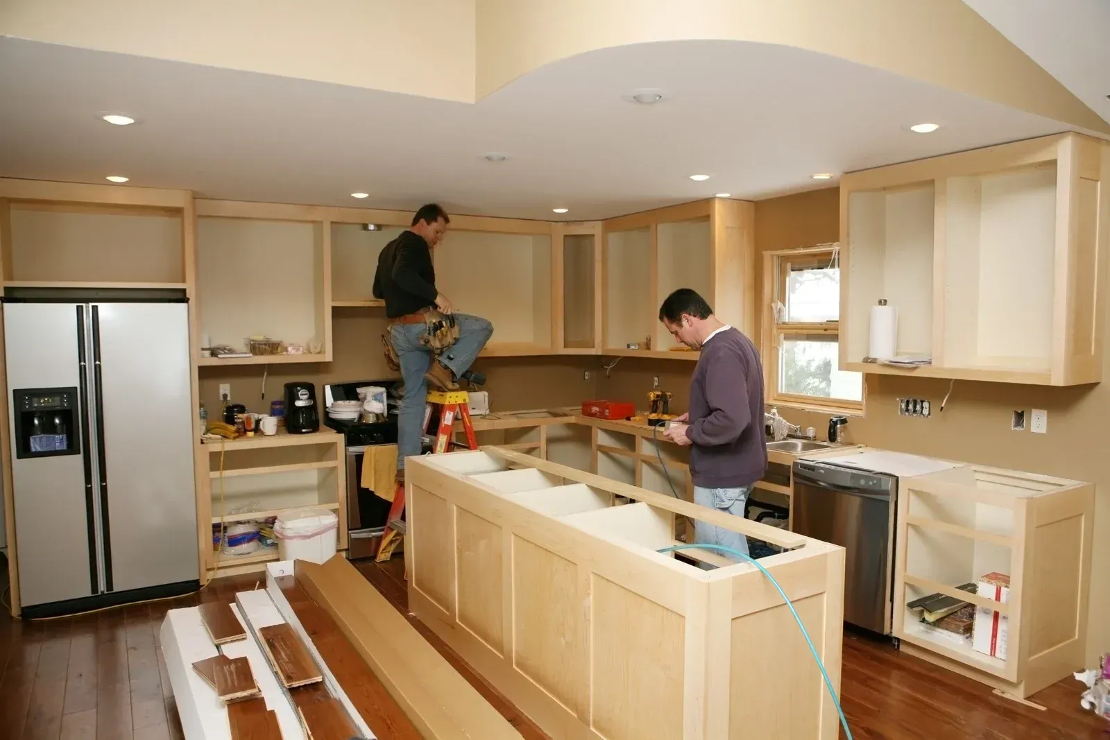 Two men are working on a kitchen with a white refrigerator
