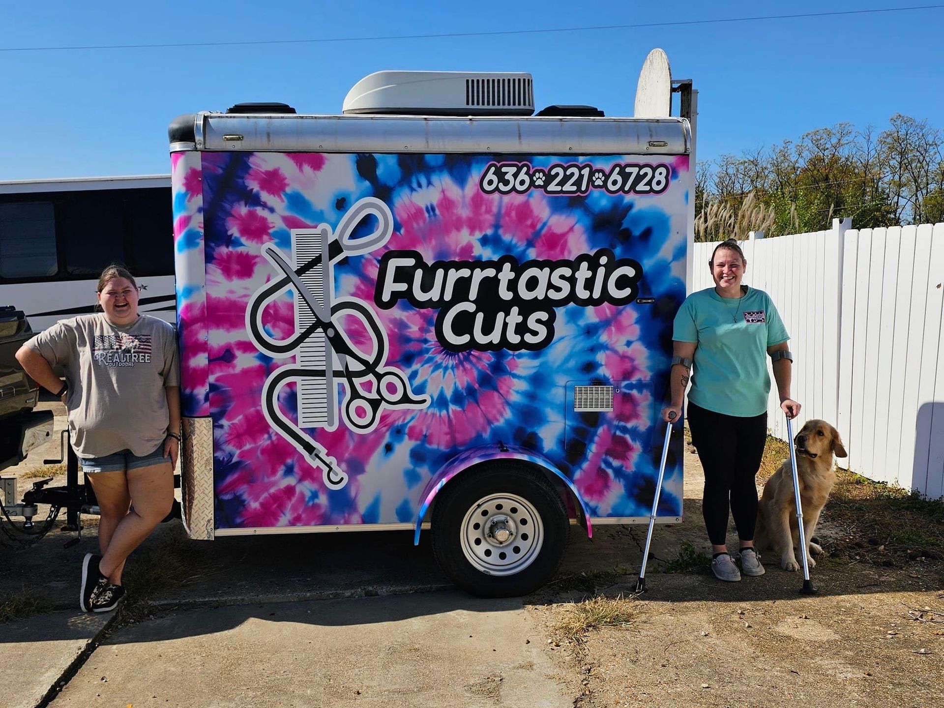 Two women standing in front of a trailer that says furrtastic cuts