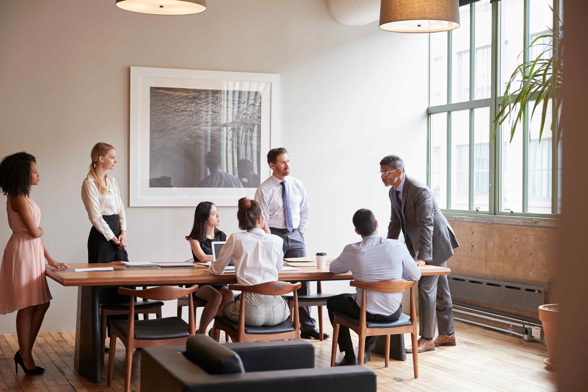 People in office meeting around a wooden table, discussing a project.