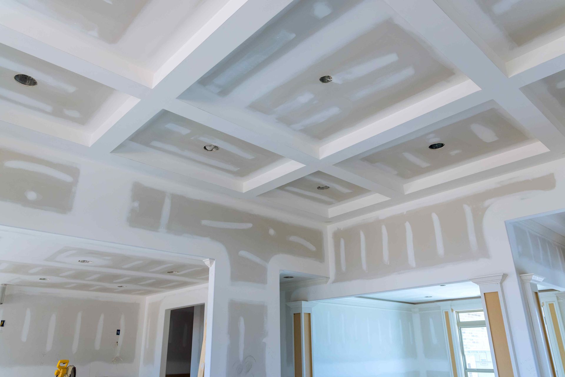 Interior room under construction, with drywall covering walls and a coffered ceiling.