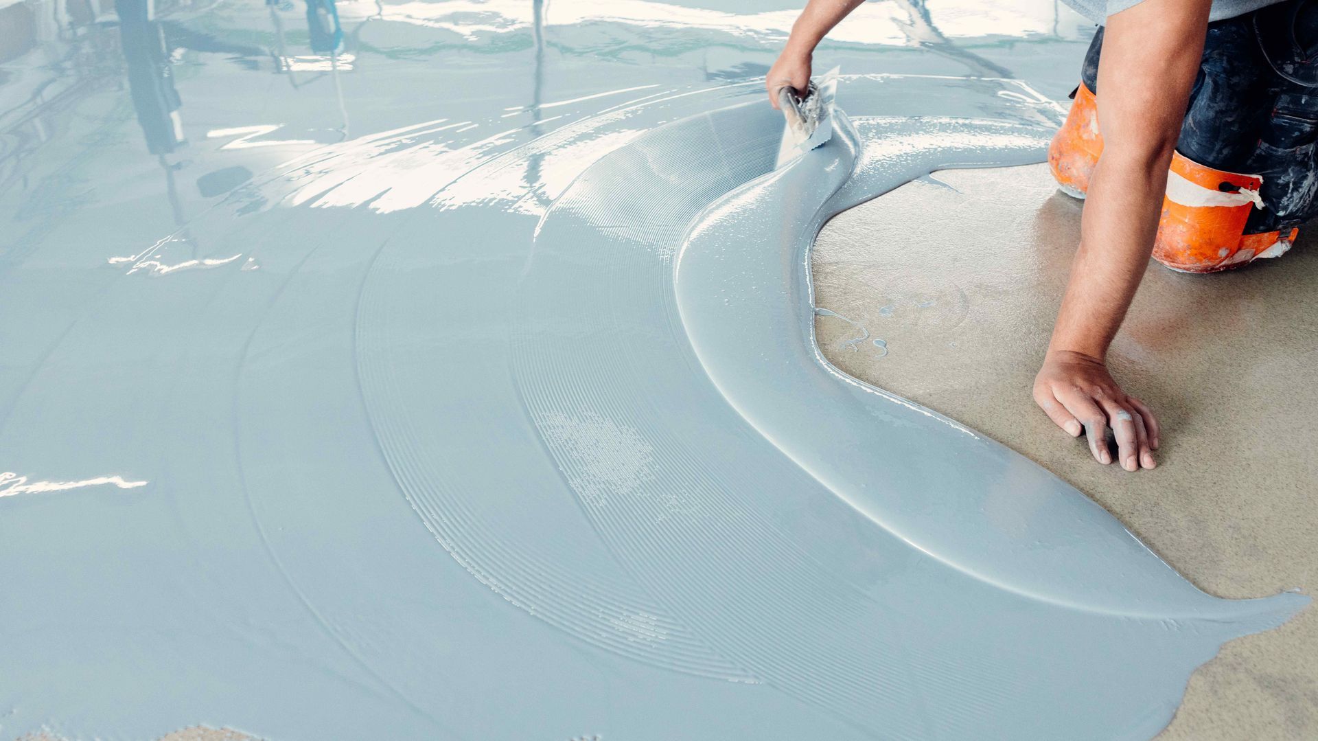 Person applying light blue epoxy flooring with a trowel.