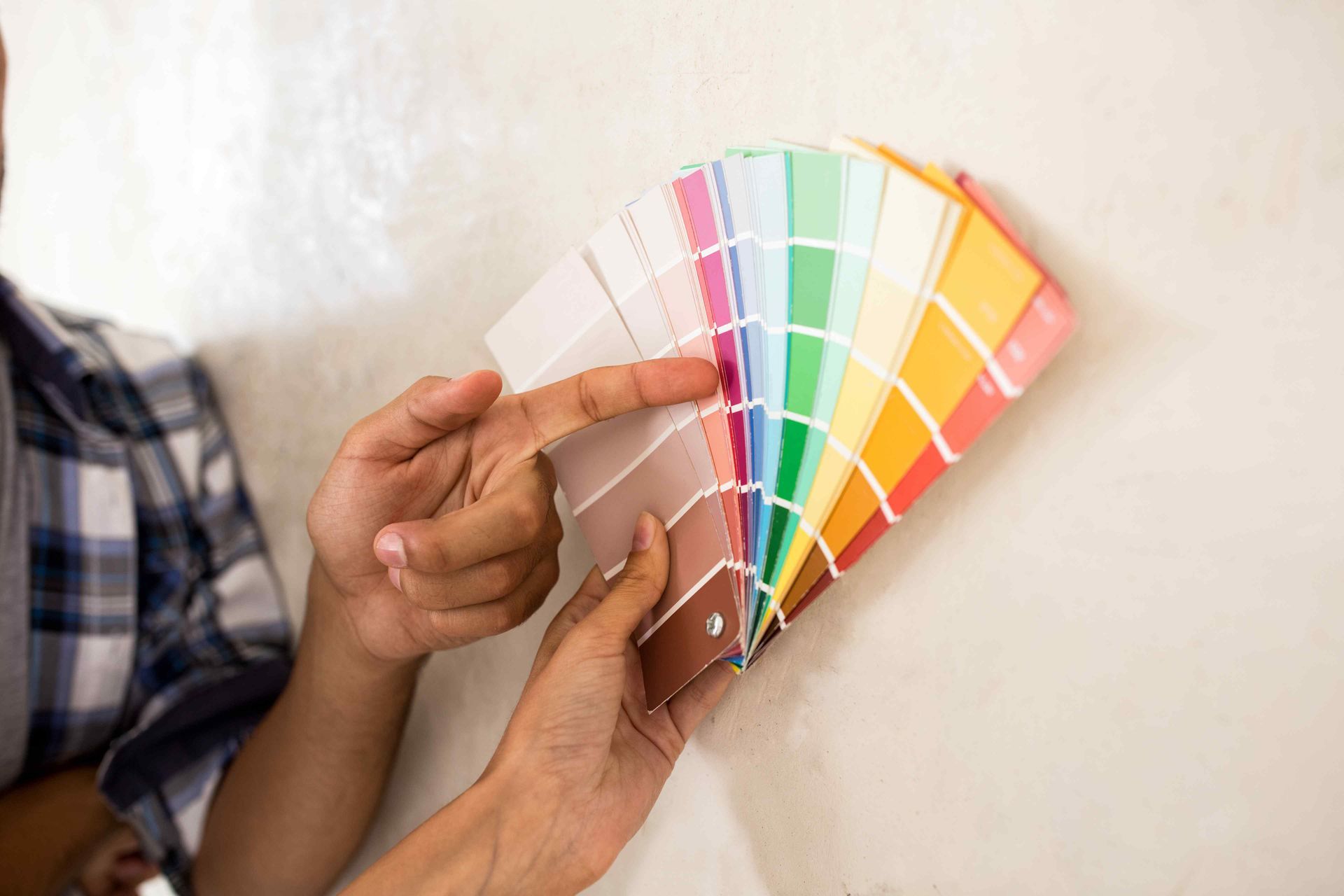 Person pointing at paint samples against a wall. The samples show a variety of colors.