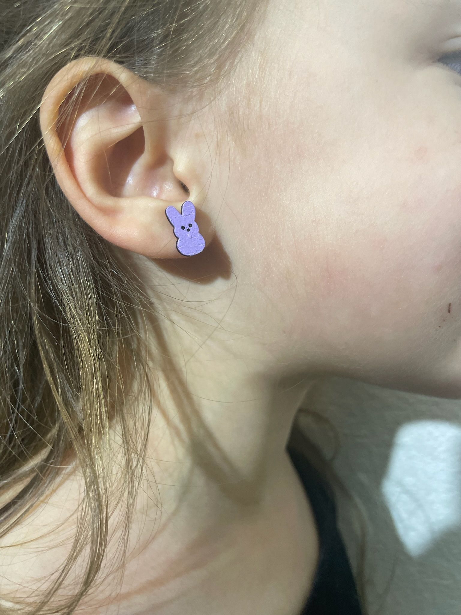A close up of a child 's ear with a pair of purple earrings.