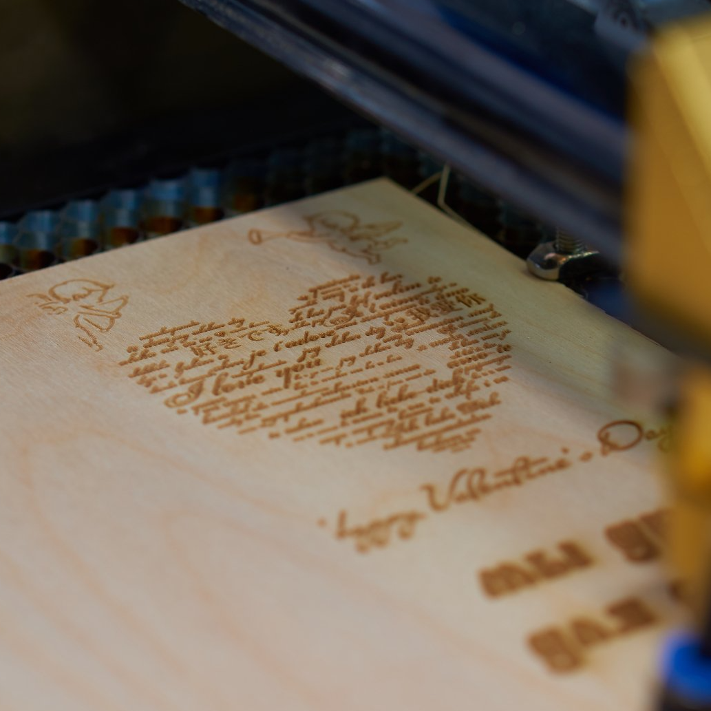 A machine is engraving a heart on a piece of wood
