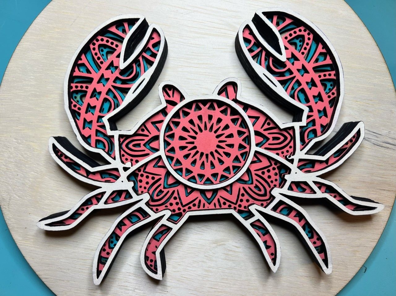A crab with a mandala design on it is on a wooden circle.