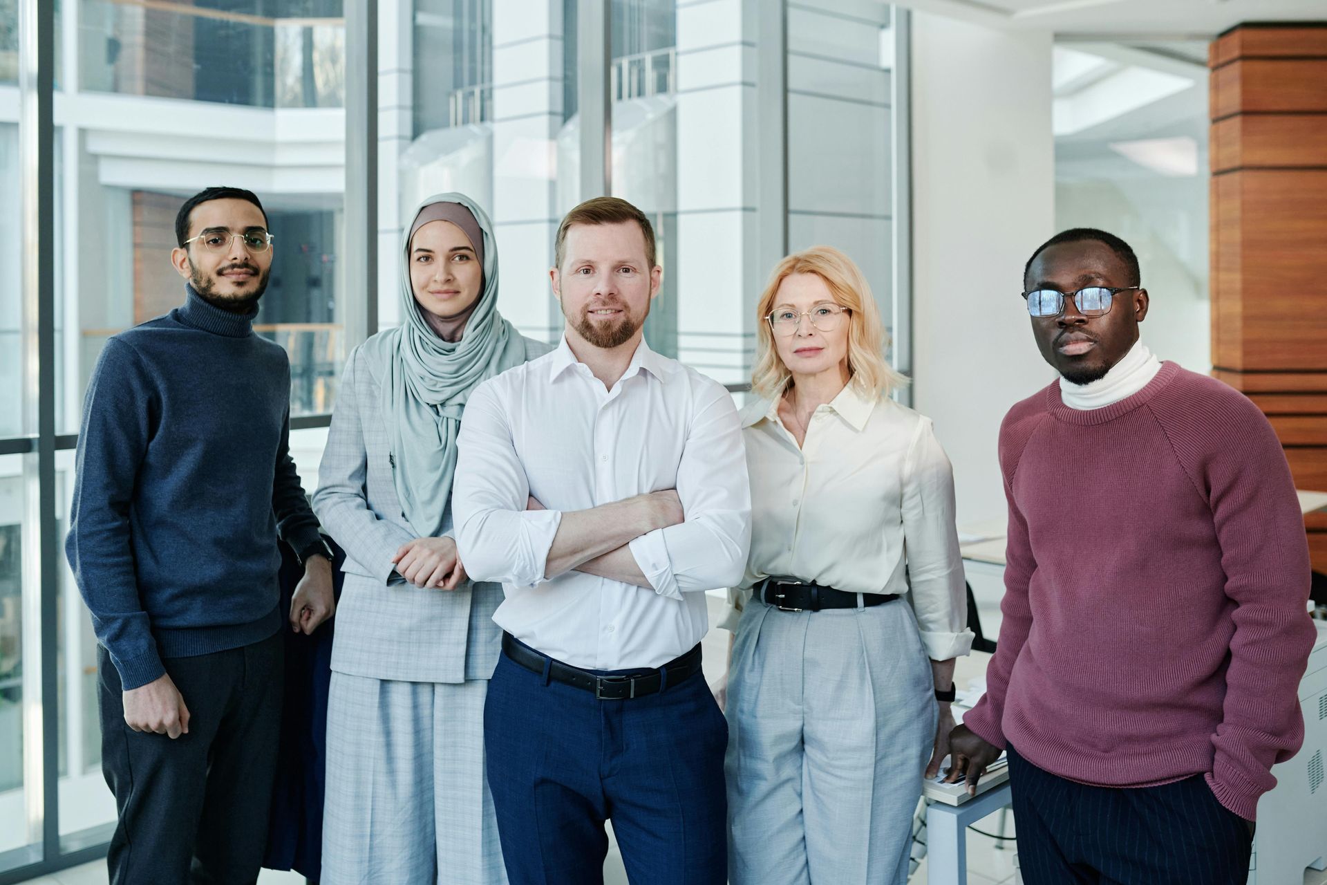 Group of five people standing in an office with a large window. They are looking at the camera.