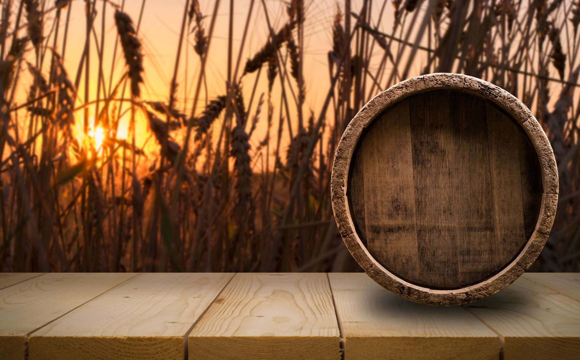 A wooden barrel is sitting on a wooden table in front of a field at sunset.