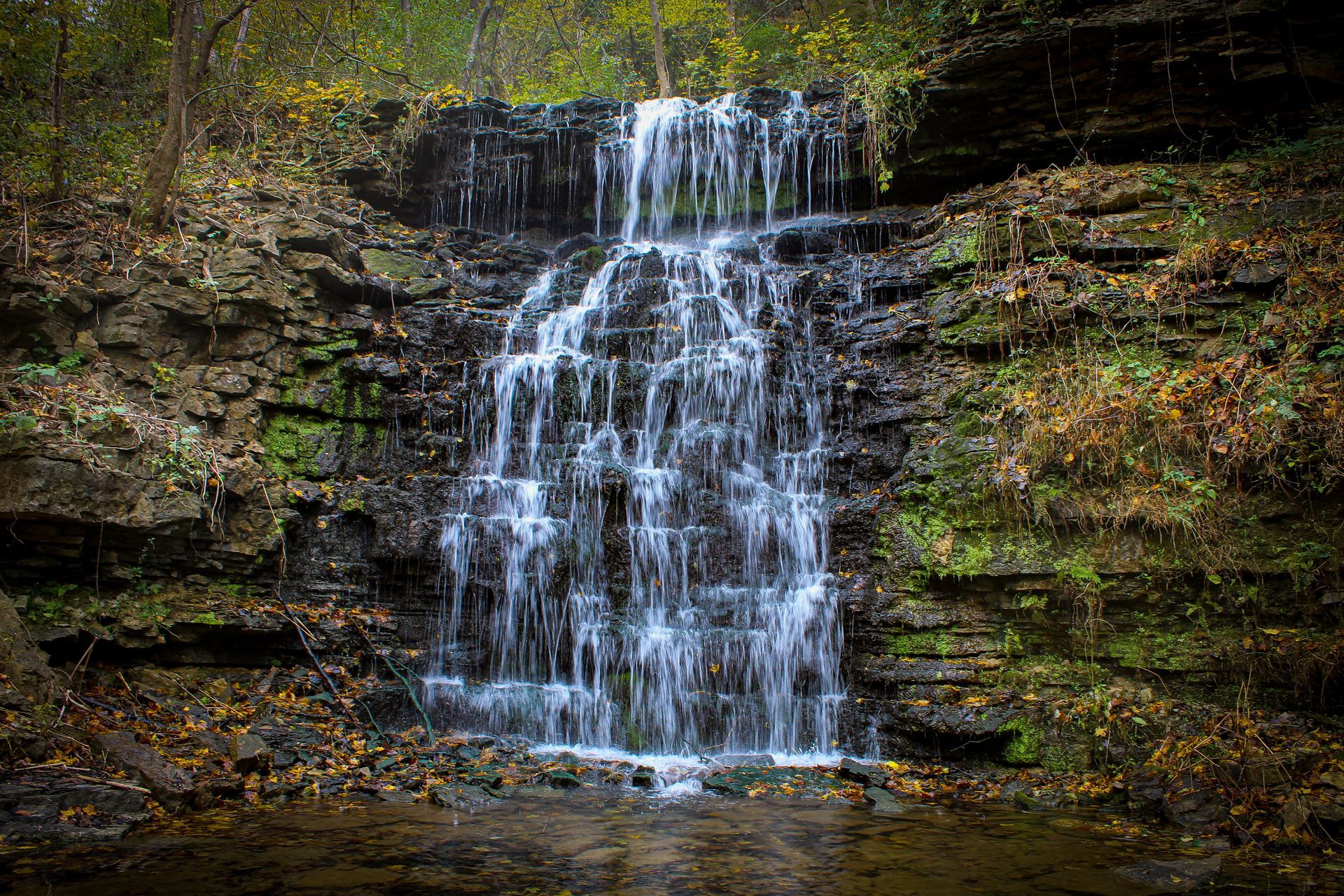 A waterfall is surrounded by trees and rocks in the middle of a forest.