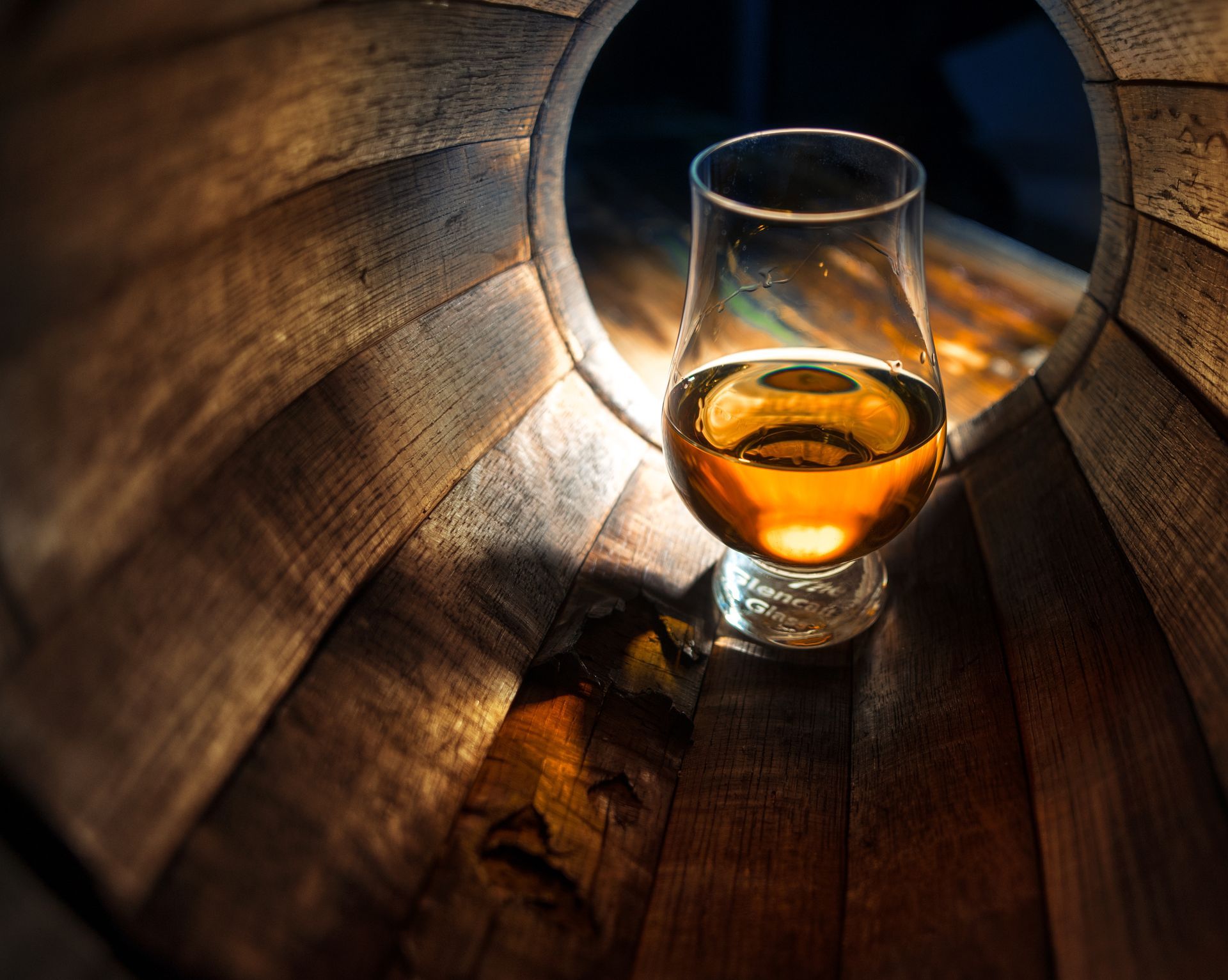 A glass of whiskey is sitting inside of a wooden barrel.