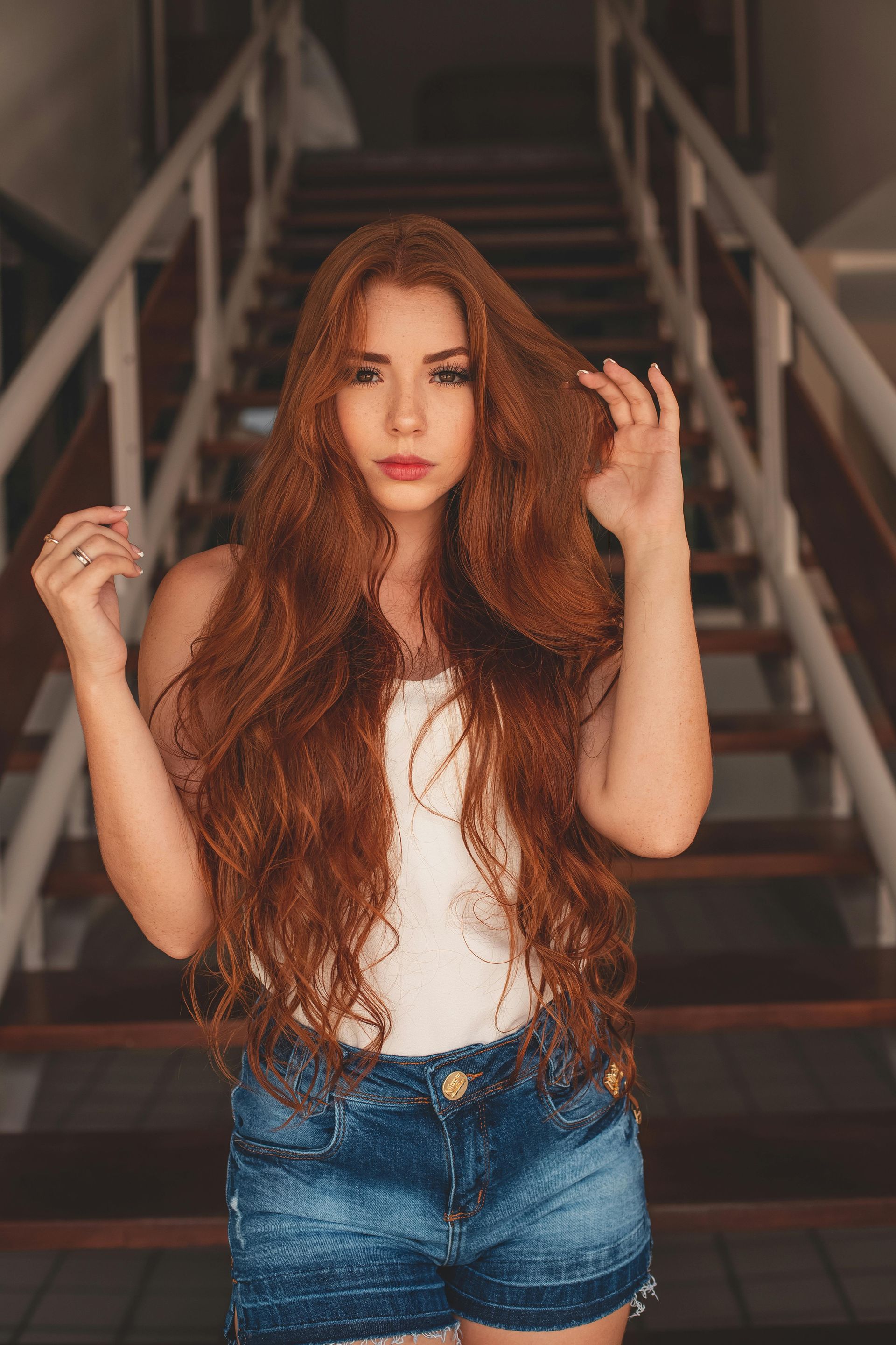 A woman with long red hair is standing on a set of stairs.