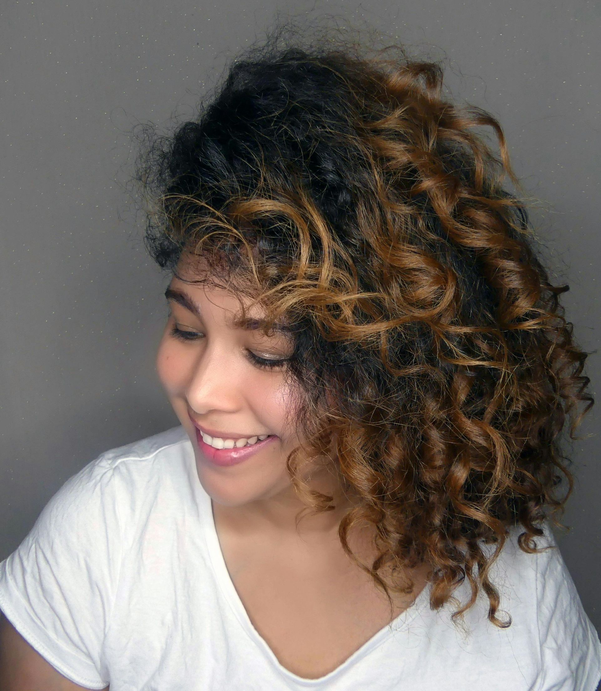A woman with curly hair is wearing a white shirt and smiling.