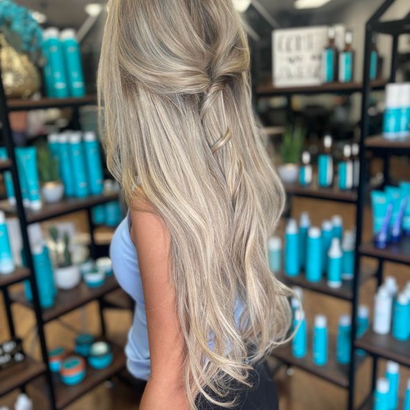 A woman with long blonde hair is standing in front of a shelf of hair products.