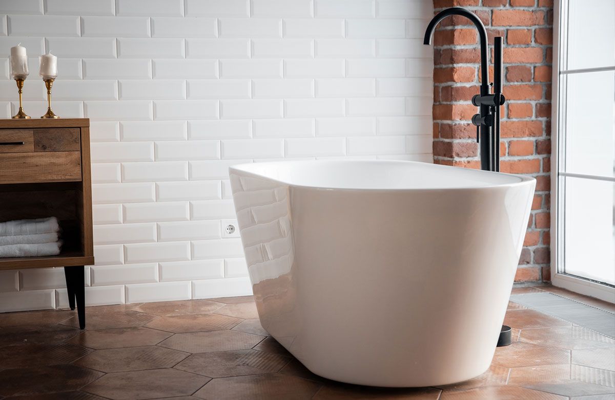 A freestanding bath against a white tiled wall