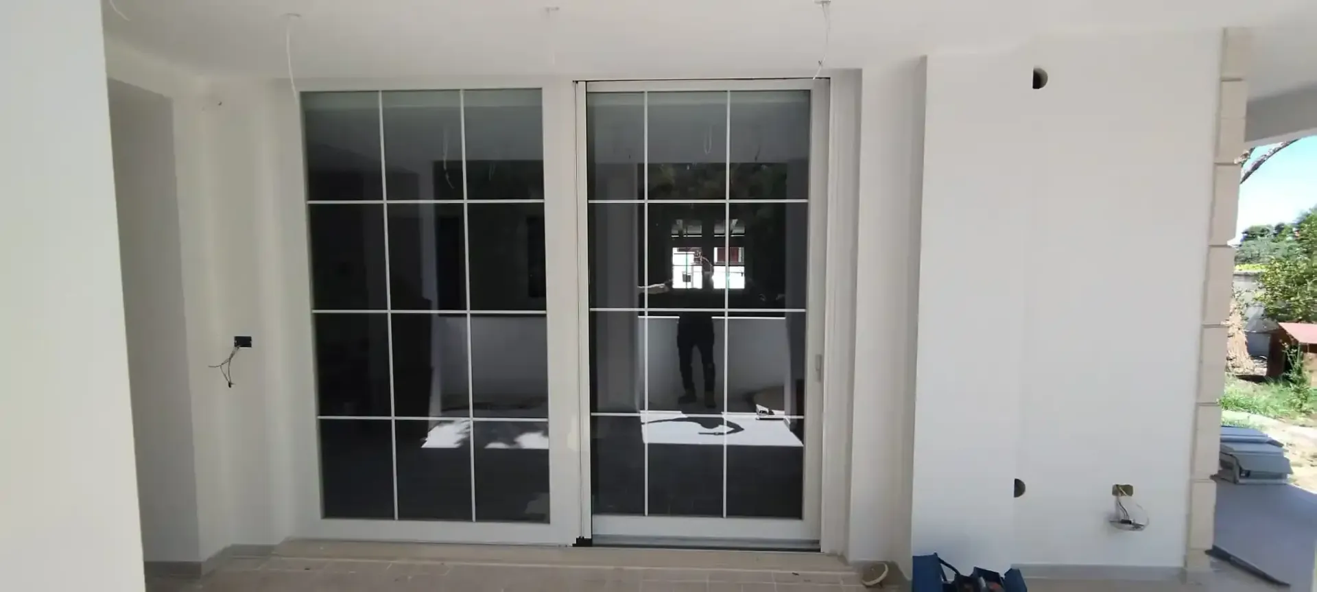 Porte scorrevoli in vetro in un edificio in costruzione, che riflettono una persona e l'interno.