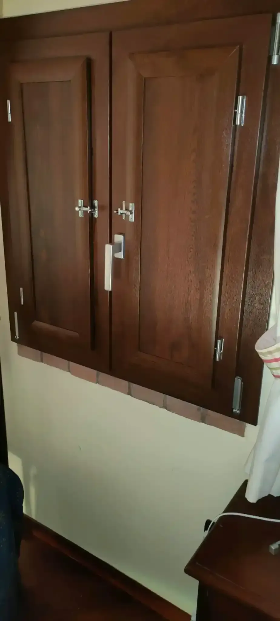 Ante in legno marrone scuro con maniglie argentate. Montate su una parete beige sopra una superficie in legno.