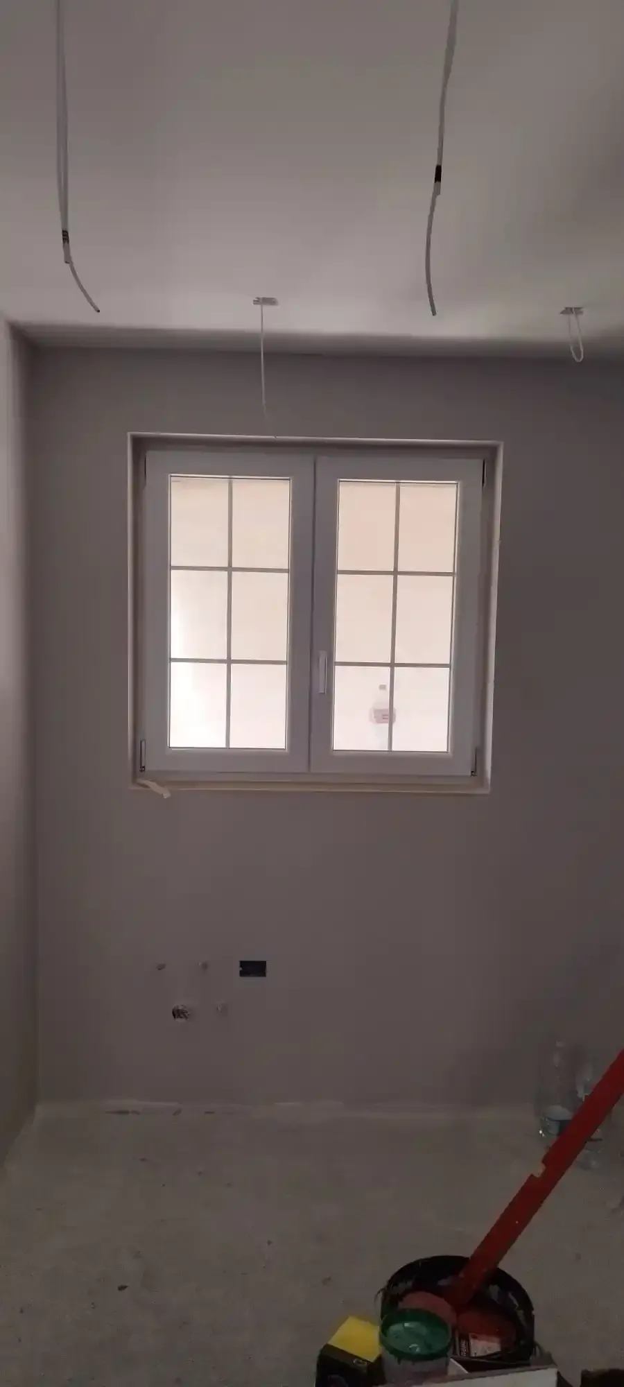 Stanza interna in costruzione con finestra e cavi elettrici a vista.