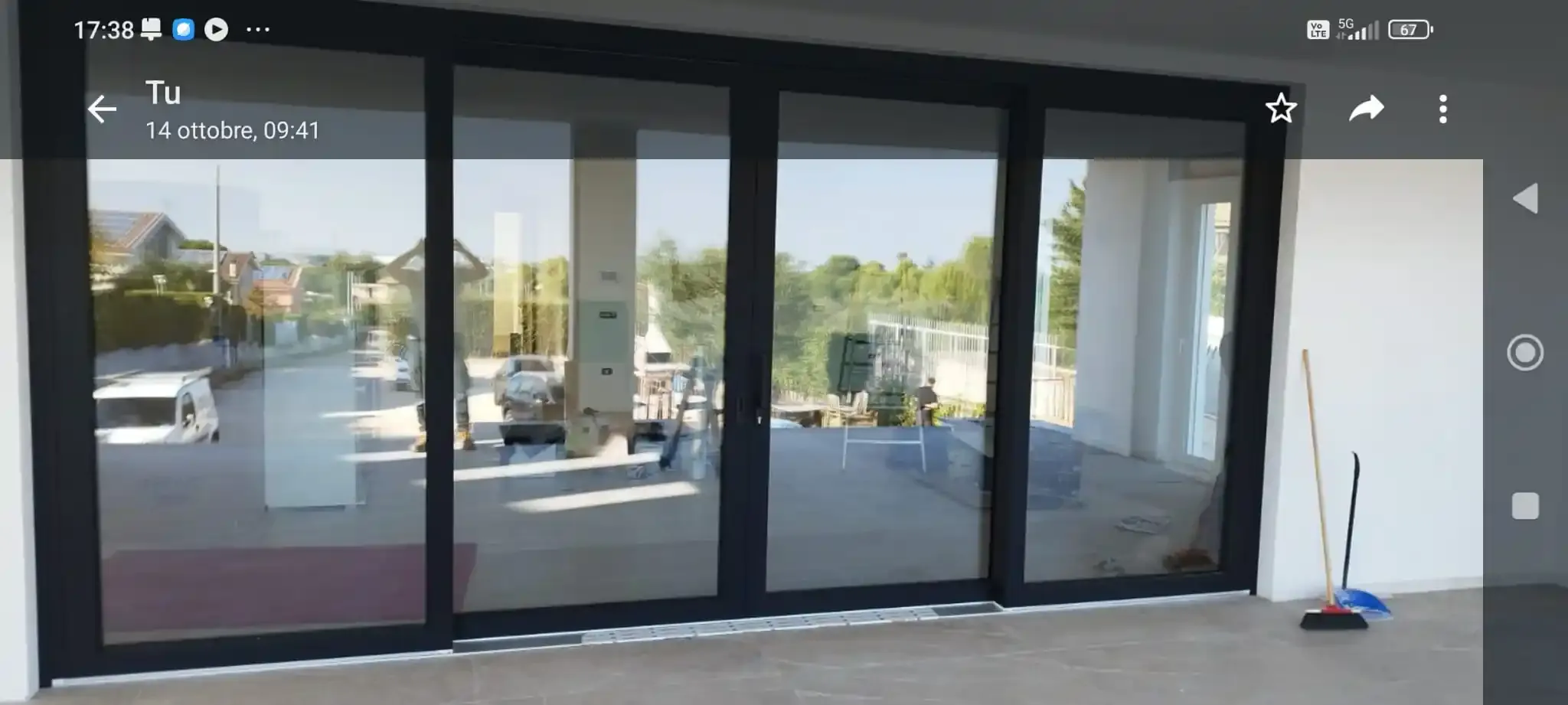 Porte a vetri che riflettono l'immagine di una stazione di servizio. Sul pavimento ci sono una scopa e una paletta.